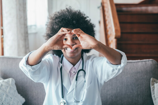 Woman Physician Doing Heart Shape Gesture With Hands. Smiling Black Female Doctor Making A Love Symbol Using Her Hands. Healthcare Worker Expressing Love And Support To Patients