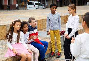 Cheerful multiethnic group of tweens spending time together on city street in warm fall day .