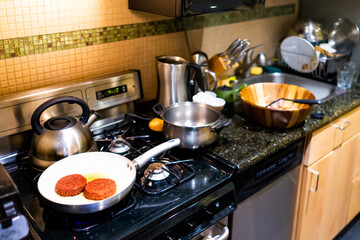 Closeup of two burger patties cooking on ceramic nonstick frying pan with kitchen interior showing appliances stove and dishwasher countertop cabinets