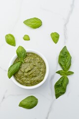 Flatlay of pesto in a bowl and basil leaves.
