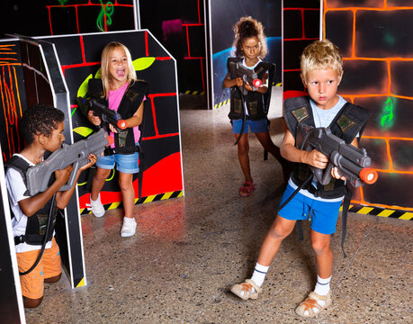 Modern preteen girls and boys of different nationalities with laser pistols playing laser tag at a dark labyrinth