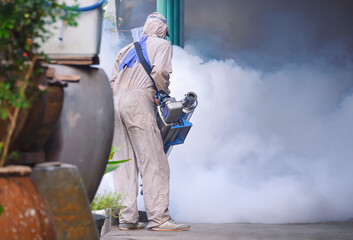 Rear view of outdoor healthcare worker using fogging machine spraying chemical to eliminate mosquitoes and prevent dengue fever on overgrown at slum area 