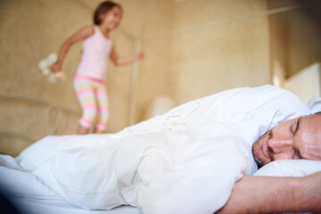 Time to wake up. Shot of a sleeping dad with his little daughter jumping on the end of the bed.