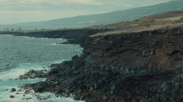 4k Aerial volcanic cliff on calm ocean Drone ib down + dolly in shot