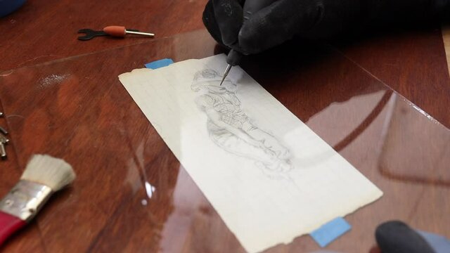 A craftsman does glass engraving with a rotary tool following a drawing on a paper