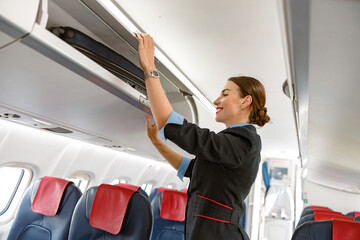 Cheerful stewardess checking overhead luggage bin in airplane