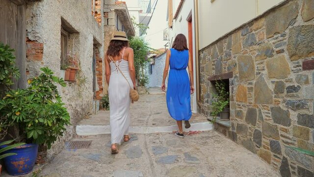 Young ladies in summer dresses are walking on a warm summer day. Two girls are walking along the Greek coast in the old town