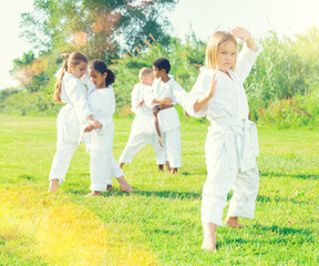 Naklejka na ściany i meble Group of children training outoors in summertime. Blonde girl standing and posing in foreground.