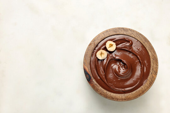 Bowl of tasty chocolate hazelnut spread on white background, top view. Space for text