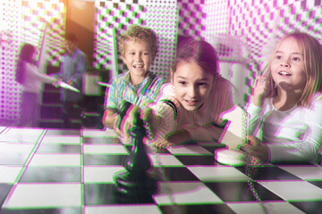 Cheerful tweens solving riddles in escape room stylized under chessboard. Toned image with...