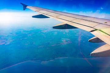 View from the airplane window at a beautiful blue clear sky, earth, sea and the airplane wing