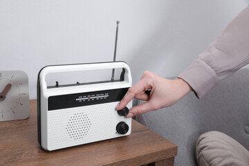 Woman turning volume knob on radio at home, closeup