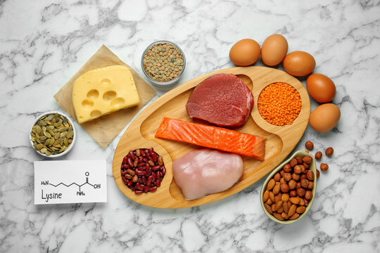 Different fresh products and paper with Lysine chemical formula on white marble table, flat lay. Sources of essential amino acids
