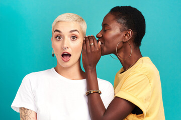 Guess what. Studio shot of a young woman whispering in her friends ear against a turquoise...