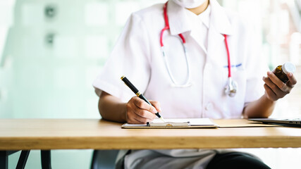 Female doctor looked at the information from the pill bottle and wrote down the details of the medication on a piece of paper.