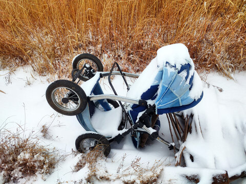 Abandoned baby stroller lying in the snow among the yellow grass