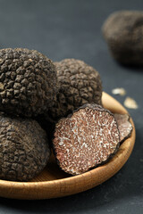 Black truffles in wooden plate on grey table, closeup