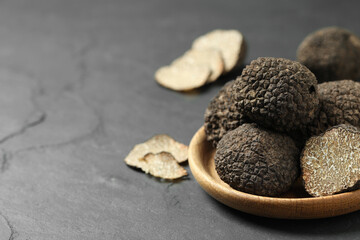 Black truffles in wooden plate on grey table. Space for text