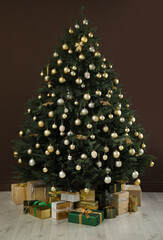 Beautifully decorated Christmas tree and many gift boxes near brown wall indoors