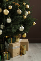 Beautifully decorated Christmas tree and many gift boxes near brown wall indoors, closeup