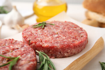 Raw hamburger patties with rosemary on wooden board, closeup