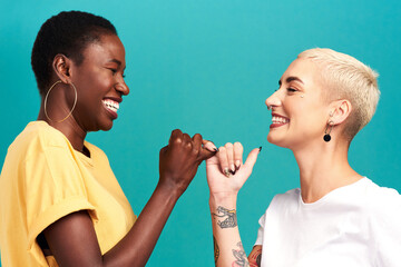 Besties forever through whatever. Studio shot of two young women linking their fingers against a...