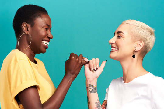 Besties forever through whatever. Studio shot of two young women linking their fingers against a turquoise background.