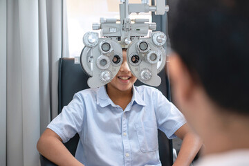 Indian boy looking through optical Phoropter during eye exam, The expert is testing the vision test with diagnostic ophthalmology equipment, selective focus