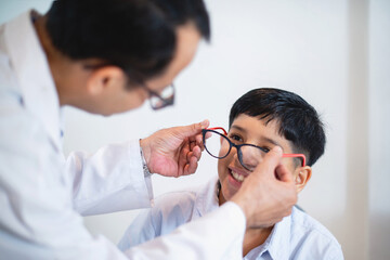 Indian optometrist or optometrist is in white coat helps to get new glasses for boy, child boy in...