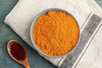 Bowl of saffron powder and spoon with dried flower stigmas on light blue wooden table, flat lay