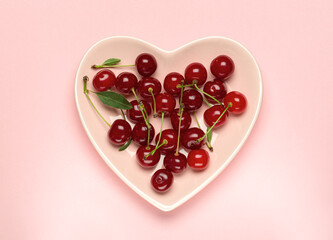 Cherries on a pink plate in the shape of a heart on a pink background.