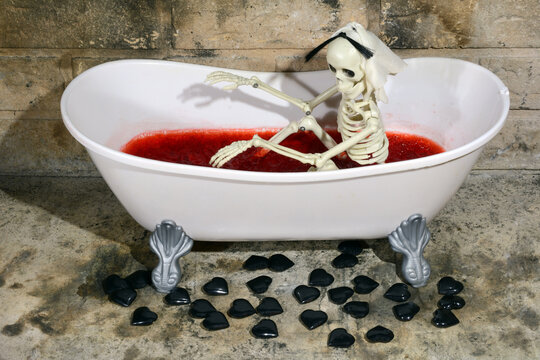 Anti-Valentine's Day skeleton in bathtub filled with blood colored raspberry gelatin and black hearts scattered on floor
