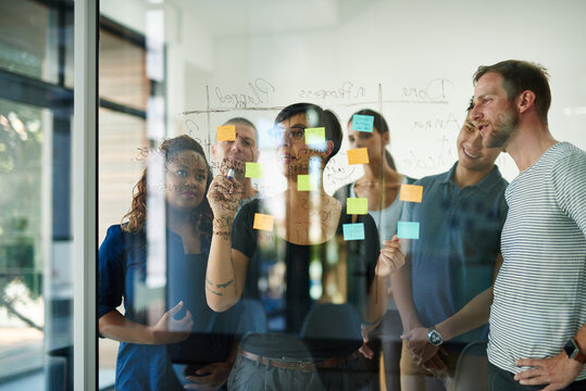 Planning is the first step. Cropped shot of a group of young designers planning on a glass board.