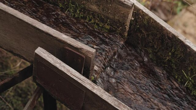 Close-up of a wooden gutter with water flowing inside. Static view