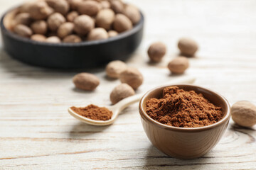 Bowl of nutmeg powder on white wooden table, space for text