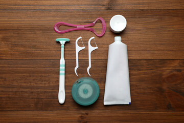 Different tongue cleaners, dental floss and toothpaste on wooden table, flat lay