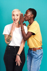For your ears only. Studio shot of a young woman whispering in her friends ear against a turquoise background.