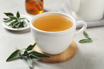 Fototapeta na wymiar Cup of aromatic sage tea and fresh leaves on light grey table
