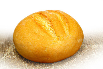Round bread with a golden crust. A loaf of bread on an abstract background of ears of corn and burlap.