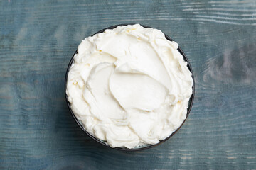 Tasty cream cheese on light blue wooden table, top view