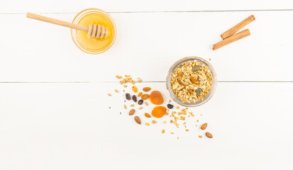 top view of a glass jar with granola and a bowl of honey. dried fruits to improve the taste. white wooden background with a copy of the space