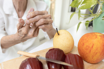 Close up of hands,old elderly cut her finger with a knife while slicing fruit in kitchen,senior...