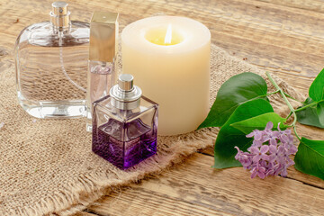Bottles of perfume, candle and lilac flowers on wooden background.