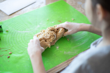 The hands of a little girl knead the dough for homemade cookies on the kitchen table sprinkled with flour.