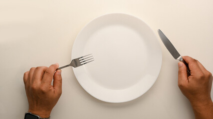 Top view image of a man holding fork and knife over dining table.