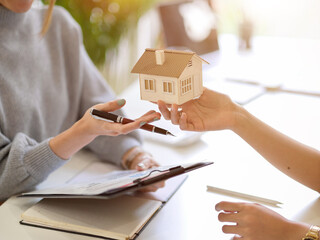 A buyer holding a house model in front of real estate agent.