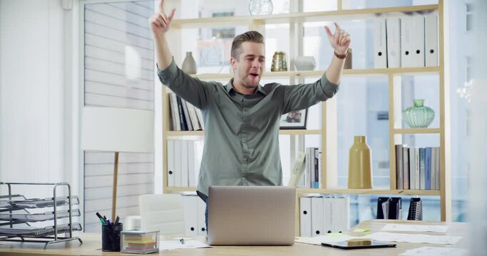 Happy young business man cheering and dancing after winning in a modern office. Confident businessman using a laptop and cheerfully celebrating success, promotion or a sale