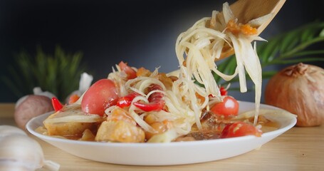 Closeup fresh yummy delicious Thai traditional popular street food spicy green papaya salad or Som Tam in white dish, person uses spoon holding chili papaya salad	