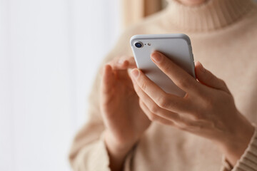 Closeup portrait of anonymous woman wearing beige casual style sweater holding mobile phone in hands, using cell phone for online communication, typing messages.