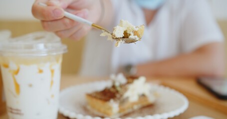 Close up woman holding eating piece of sweet dessert cake on the table at cafe	
